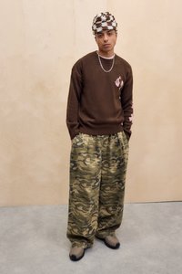 Brauner Pullover mit hellrosa Akzenten und Tarnhosen, mit entspannter Passform, dazu eine gestrickte braun-weiße Mütze.