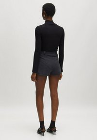 Zwarte geribbelde lange mouwen top gecombineerd met hooggeplaatste grijze shorts, die een getailleerde pasvorm laten zien met een gladde textuur en minimale details.