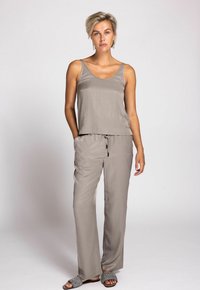Woman standing wearing taupe satin sleeveless top and matching drawstring pants with woven black-and-white slip-on sandals.