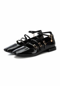 Bailarinas de charol negro con punta afilada, múltiples correas cruzadas y acentos de hardware en tono dorado. Tacón bajo cuadrado para mayor soporte.