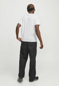 Hvid bomulds t-shirt parret med sorte cargo bukser, der har sidelommer og en afslappet pasform. Brun kasket med justerbar strop, sorte sneakers.