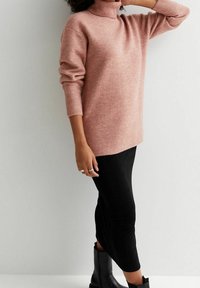 Maglione turtleneck rosa a maglia con vestibilità morbida e polsini a coste, abbinato a una gonna nera aderente e stivaletti alla caviglia. Texture morbida in generale.