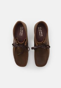 Barna bőr cipők lekerekített orral, barna fűzőkkel és alacsony profilú kialakítással. A belső részén fehérrel van nyomtatva a "CLARKS ORIGINALS" felirat.
