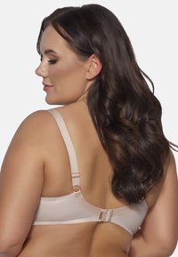 Reggiseno beige con spalline regolabili, dotato di chiusura con gancio e occhiello, texture liscia e dettagli delicati sulla fascia e le spalline.