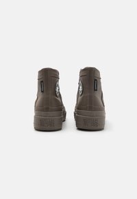 Adidași înalți impermeabili de culoare maro, cu piele texturată, cusături în contrast, gleznă curbată și talpă din cauciuc cu logo-ul mărcii ridicat.