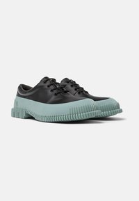 Zapatos de cuero negro con una suela de goma verde menta, que presenta un diseño texturizado y estriado. Cierre con cordones y puntera redondeada.