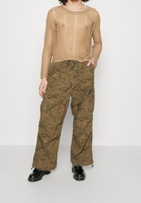 Beige stickad topp med en lös, öppen väv, tillsammans med bruna, mönstrade cargobyxor med dragsko i midjan och avsmalnande muddar.