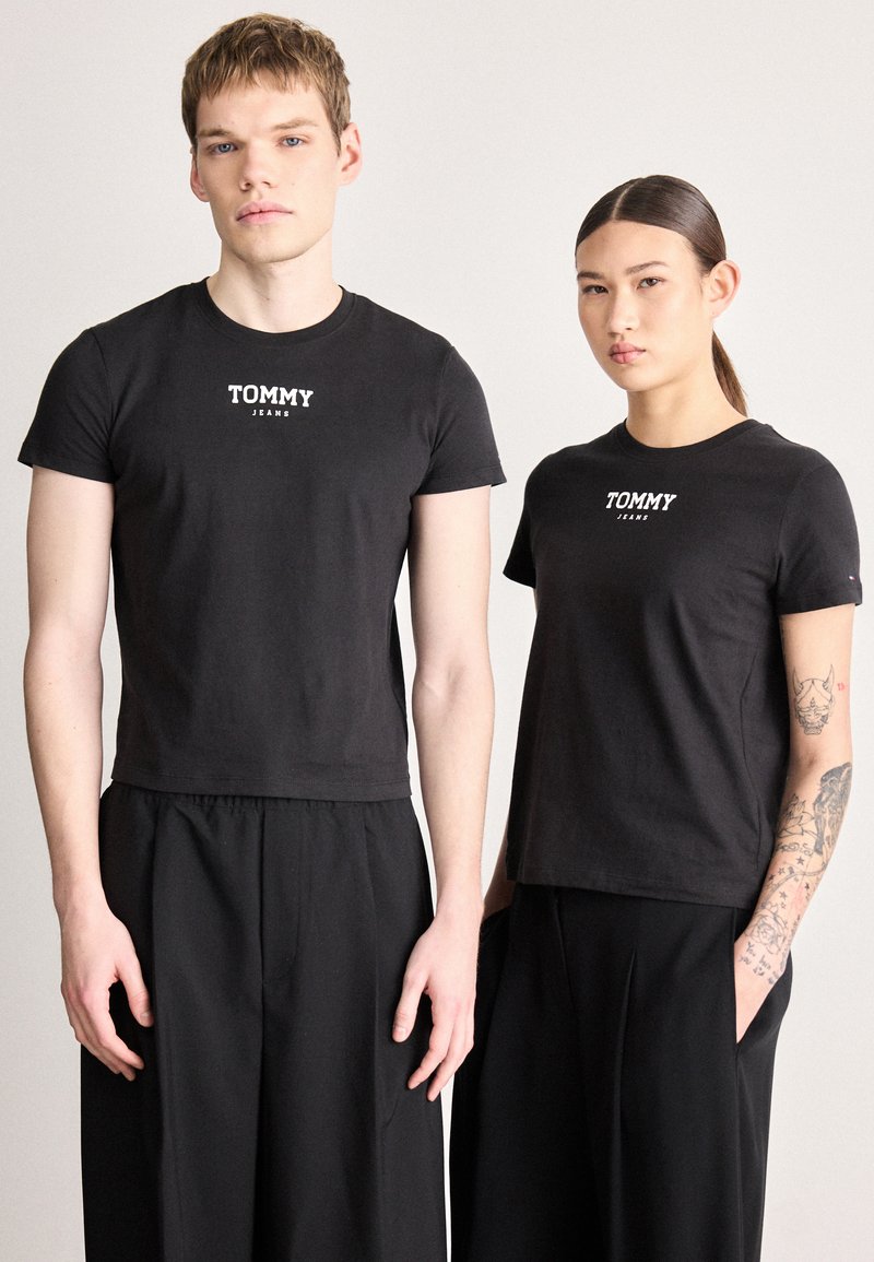 T-shirts pretas de algodão com mangas curtas e gola redonda, com o logótipo branco "TOMMY JEANS" no peito. Combinadas com calças pretas.