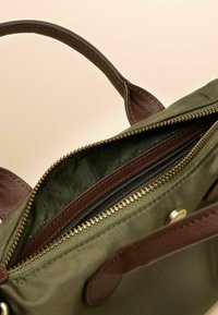 Olivovo zelená látková taška s hnedými textúrovanými rukoväťami a zipsami. Vnútri je zelená podšívka s malými zlatými bodkami a niekoľkými priehradkami.