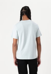 Himmelblaues T-Shirt mit kurzen Ärmeln aus Baumwolle, mit Rundhalsausschnitt und lockerer Passform, von hinten vor einem schlichten Hintergrund betrachtet.