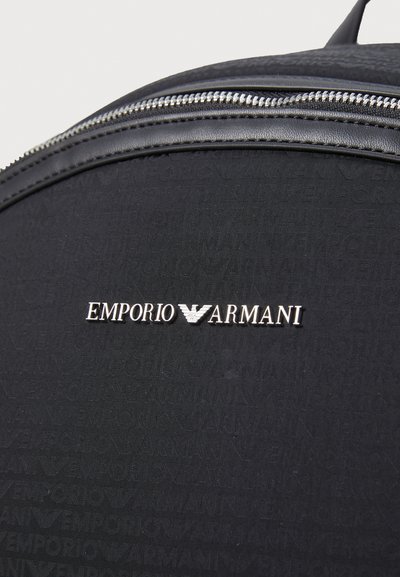 Rucsac negru cu o textură netedă, având un logo embosat argintiu "EMPORIO ARMANI" și un model repetitiv. Detalii despre închiderea cu fermoar sunt vizibile.