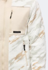 Μπεζ και λευκό fleece μπουφάν με ανοιχτοκαφέ λεπτομέρειες, με φερμουάρ σε τσέπη στο στήθος και πλαϊνή τσέπη με μαύρα κορδόνια φερμουάρ.