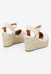 Sandalias de cuña de esparto beige con una correa de tobillo de tela texturizada, punta redonda y tacón de yute trenzado. Presentan un cierre de hebilla.