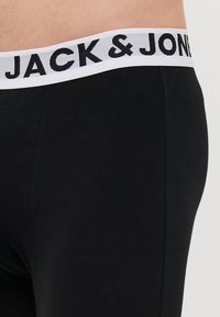 Schwarze Baumwoll-Boxershorts mit einem weißen elastischen Bund, auf dem "JACK & JONES" in Schwarz bedruckt ist. Glatte Textur, körpernahe Passform.