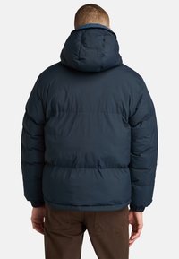 Marineblå pufferjakke med stor hætte, elastiske manchetter og kviltet design for isolering, med en glat, mat finish.