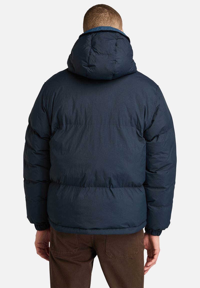Die marineblaue Steppjacke verfügt über eine große Kapuze, elastische Bündchen und ein gestepptes Design zur Isolierung, mit einer glatten, matten Oberfläche.