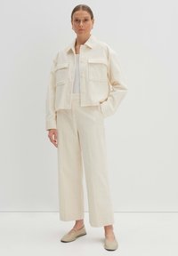 Cremige kordjacke mit zwei vorderen Taschen kombiniert mit passenden weiten Hosen. Verfügt über einen Kragen und lange Ärmel. Schuhe mit Satinfinish.