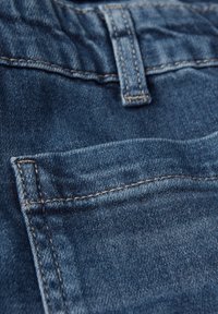 Džínové kalhoty v tmavě modré barvě s viditelným šitím. Obsahují malou přední kapsu a texturovaný povrch látky.