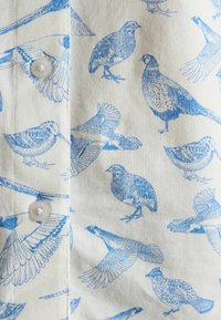 Belo blago z modrimi ptičjimi ilustracijami v različnih pozah in dvema belima gumboma, vidnima ob navpični šivi.