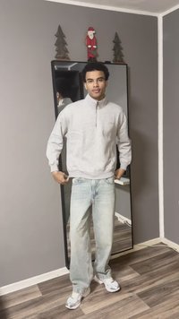 Ελαφρώς γκρι ζακέτα με φερμουάρ, άνετα ξεβαμμένα μπλε τζιν και λευκά αθλητικά παπούτσια. Καθρεφτισμένο φόντο με μινιμαλιστική διακόσμηση.