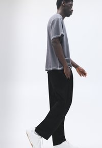 Grijze t-shirt met contrasterende witte stiksels, gecombineerd met losse zwarte broek en witte sneakers, wat een casual outfit creëert.