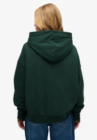 Zielona bluza z kapturem, luźnego kroju, z prążkowanymi mankietami i zakończeniem. Miękka tkanina, minimalistyczny design bez widocznych logo ani wzorów.