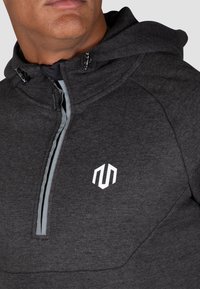 Felpa grigia con cappuccio, colletto alto, zip frontale e rivestimento interno grigio a contrasto. Presenta un logo bianco sul petto e cordini regolabili.