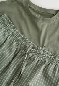 Olivenfarbiges T-Shirt mit rundem Ausschnitt, kombiniert mit helloliven gestreiften Shorts mit elastischem Taillenbund und Kordelzug.