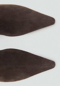Semelles de chaussures en daim marron avec une forme étroite et allongée et une texture lisse ; présente une couture le long du centre.