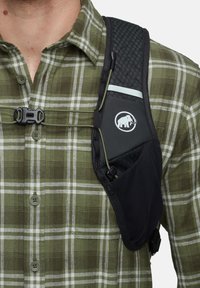 Zwarte accessoireharnas met een gaasstructuur, groene accenten, verstelbare banden en logo. Draagover een groen geruit overhemd met witte lijnen.