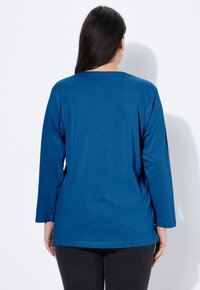 Koszula z długim rękawem w jednolitym niebieskim kolorze, z okrągłym dekoltem i luźnym krojem, wykonana z miękkiej bawełnianej tkaniny o minimalnej fakturze.