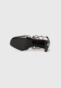 Svart högklackad sandal med en snurrad remdesign och klack i blockform. Sulan är slät och platt med en elegant finish.