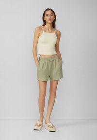 Lichtbeige aansluitend tanktop gecombineerd met groene geweven shorts met een elastische tailleband en zijzakken. Platformsandalen in een neutrale tint.