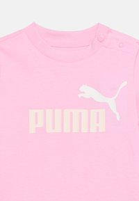 Ροζ παιδικό μπλουζάκι με στρογγυλή λαιμόκοψη, κουμπιά τύπου snap στον ώμο και λευκό λογότυπο Puma με γραφικό αλτικό γατί στο στήθος.