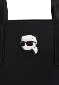 Borsa nera con un emblema lucido in stile cartone animato, dotato di occhiali da sole e coda di cavallo, realizzata in pelle e tessuto con un design strutturato.