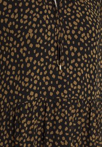 Musta kangas, jossa on hajanaisesti beige leopardikuvio, röyhelöreuna ja solmittava avonainen pääntie.