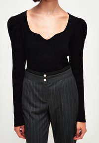 Czarny, prążkowany top z długim rękawem, głębokim wycięciem typu scoop i bufkami na ramionach, w połączeniu z szarymi spodniami w prążki z dwoma guzikami z przodu.