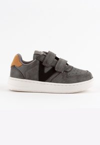 Zapatilla de cuero gris con dos correas de velcro, suela de goma blanca y acento de ante naranja en el talón. Presenta perforaciones en la puntera.