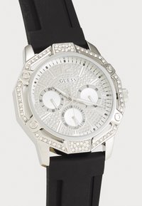 Reloj analógico plateado con caja octogonal, correa de goma negra, esfera brillante, tres subesferas y acentos de cristal en el bisel y la correa.
