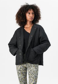 Giacca nera trapuntata con chiusura a pressione, dotata di ampie tasche e vestibilità comoda. Abbinata a pantaloni a stampa leopardo per un contrasto.