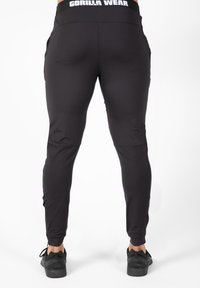 Zwarte sportleggingen met een aansluitend ontwerp, elastische tailleband, ritszakken en logodetails op de taille en onderbenen.