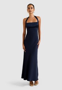 Vestido de noite azul-marinho com decote halter, corpo justo e saia fluida. Tecido suave com um brilho sutil, realçando a silhueta elegante.