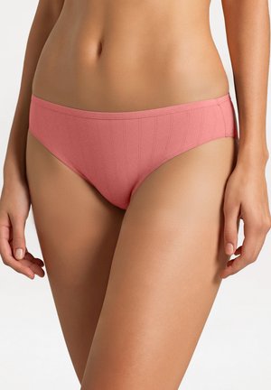 Femme portant un sous-vêtement bikini côtelé rose, vue de la taille jusqu'au milieu de la cuisse sur un fond uni.