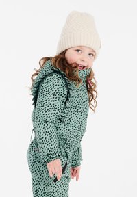 Groene sneeuwpak met een dessin van zwarte stippen, een gerimpelde kraag en elastische manchetten. Gecombineerd met een crèmekleurige gebreide muts met een gestructureerd patroon.