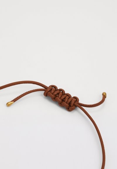 Braunes Lederband mit einem geknoteten Design in der Mitte, das zwei glatte Enden und eine metallische Spitze in goldfarbener Ausführung aufweist.
