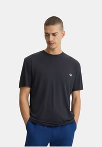 T-shirt a girocollo blu scuro, maniche corte, in tessuto morbido, con un piccolo logo sul petto, abbinato a pantaloni blu.