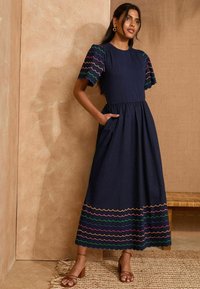 Abito blu navy con maniche corte, decorato con un ricamo a scallop colorato, corsetto aderente, gonna svasata e tasche laterali.