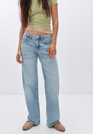 Brede blauwe jeans van denim, lichte wassing, met een relaxte pasvorm. Gecombineerd met een strakke olijfgroene top en bruine instappers.