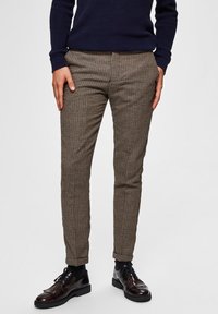 Rutiga bruna byxor med slim fit, med subtil textur. Parat med glänsande svarta snörskor, vilket fulländar en skräddarsydd look.