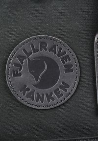 Кръгла черна кожена лепенка с релефна глава на лисица и текст "Fjällräven Kånken" върху тъмен текстуриран плат.